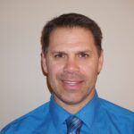 Smiling man in blue shirt and tie headshot