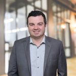 Man in gray blazer smiling in office hallway