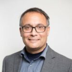 Smiling man wearing glasses and gray blazer