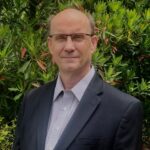 Man in suit and glasses outdoors by greenery