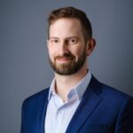 Professional headshot of bearded man in blue suit