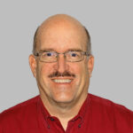 Smiling bald man with glasses and mustache, red shirt