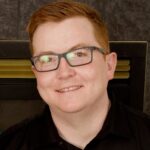Smiling person with red hair and glasses indoors