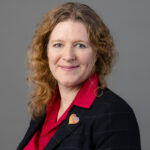 Professional headshot of woman in red blouse and blazer