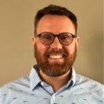 Smiling bearded man wearing glasses and blue shirt