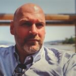 Bald bearded man in button-down shirt outdoors