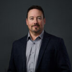 Professional headshot of man in blazer and gray shirt