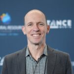 Smiling bald man in blazer at event backdrop